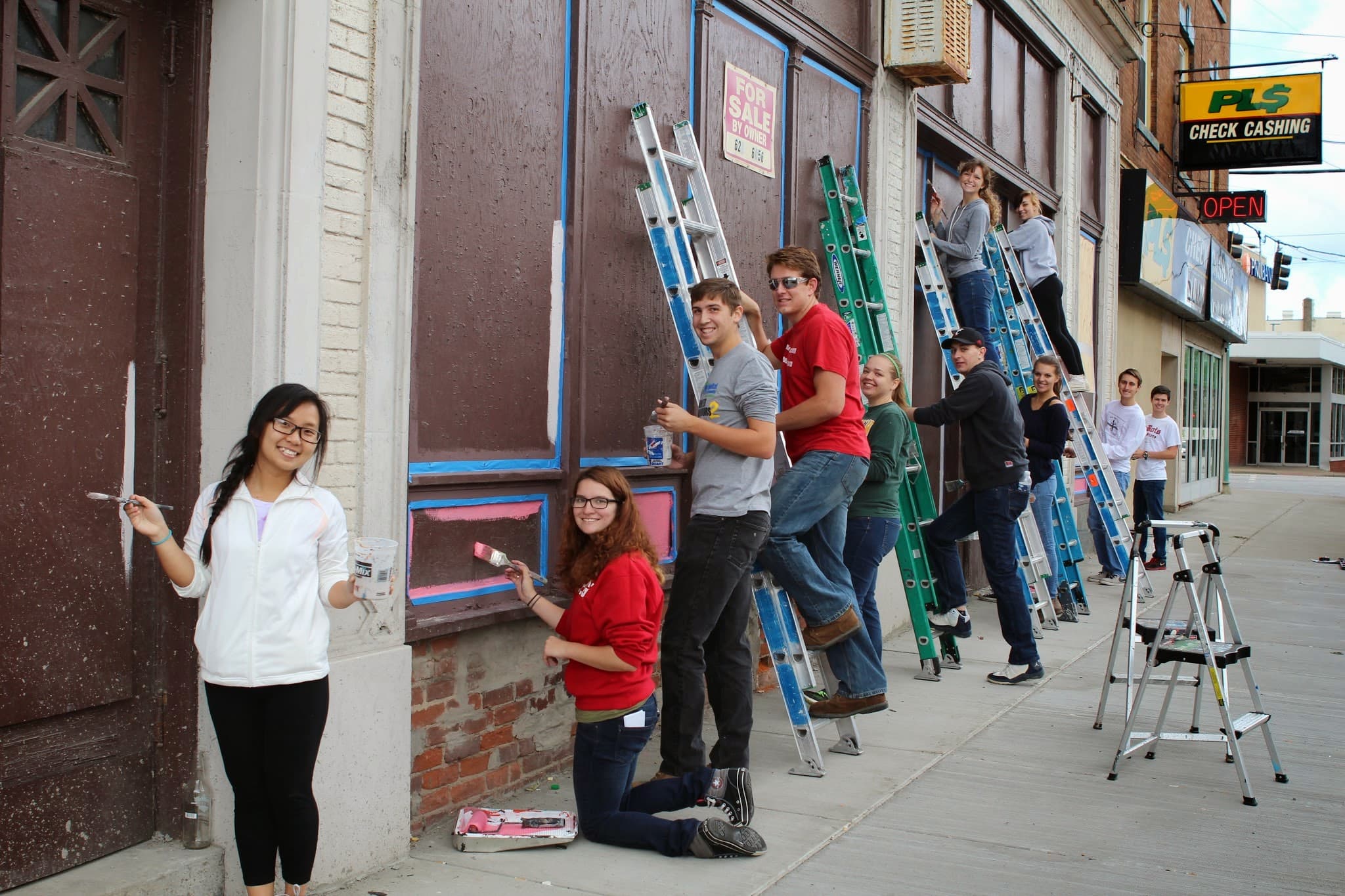Volunteers painting a bright mural onto a long exterior wall at Walnut Hill, smiling as they work along the scaffold line.
